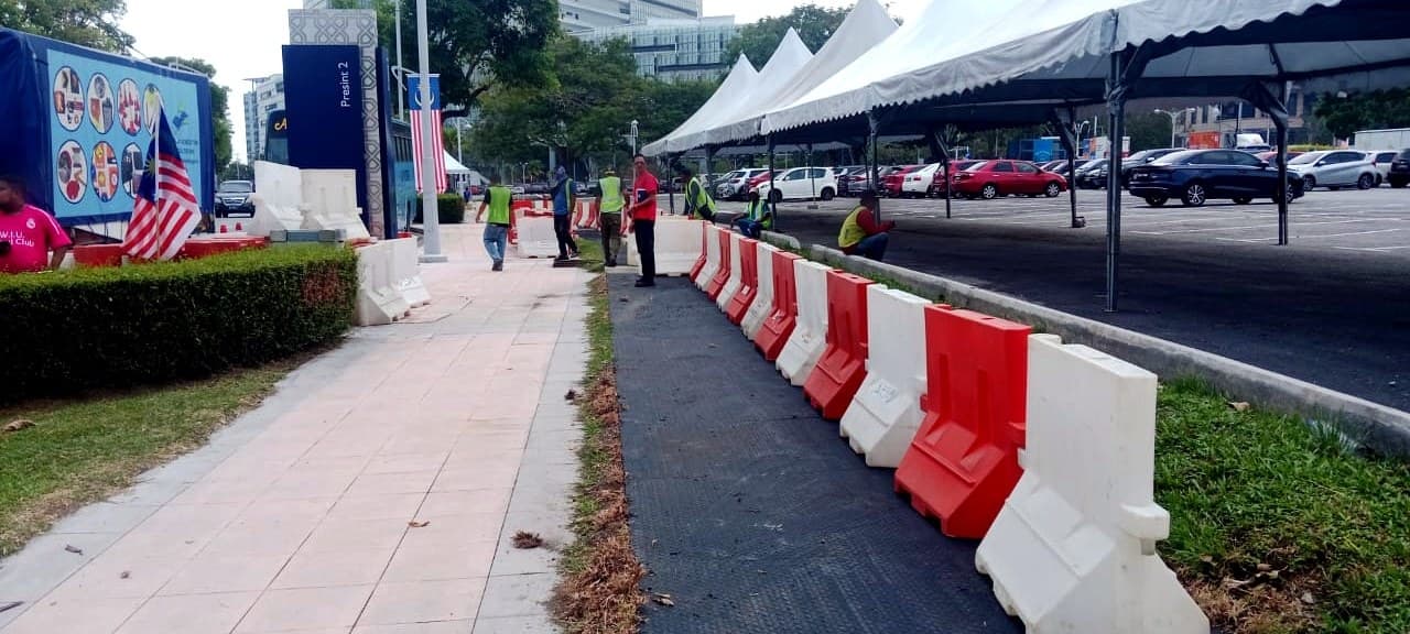 Cone Rental的红白塑料道路护栏沿布城一场公共活动的行人通道排列,背景为活动帐篷与马来西亚国旗。马来西亚活动交通管理与道路封闭设备租赁。